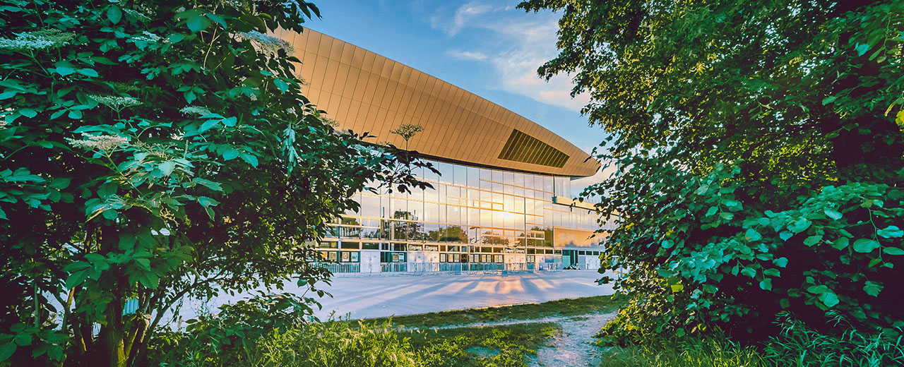 Fassade der Max-Schmeling-Halle mit grünem Park davor.